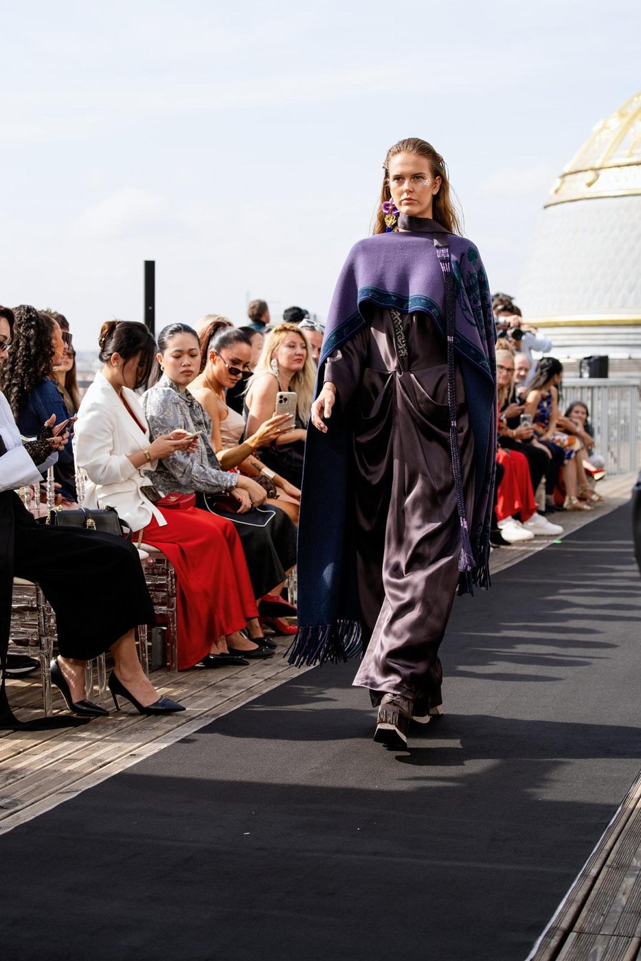 Mannequin défilant en cape violette, cristaux sur le visage