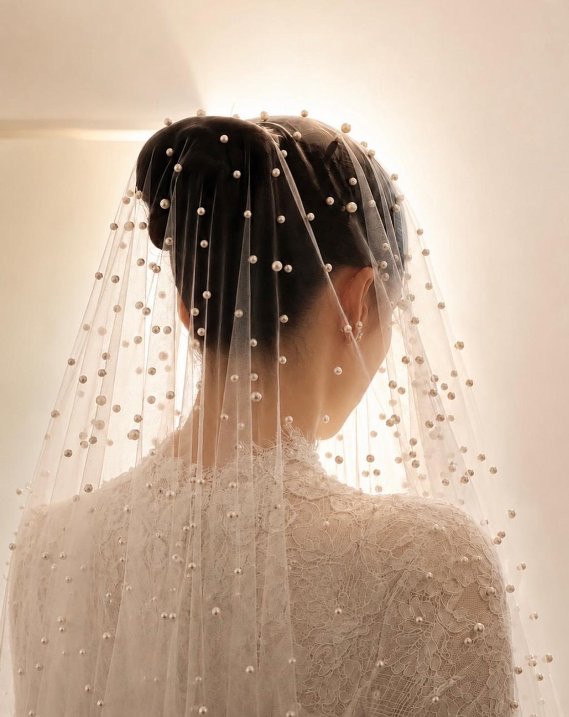 Voile de perles sur un chignon de mariée, robe en dentelle vue de dos