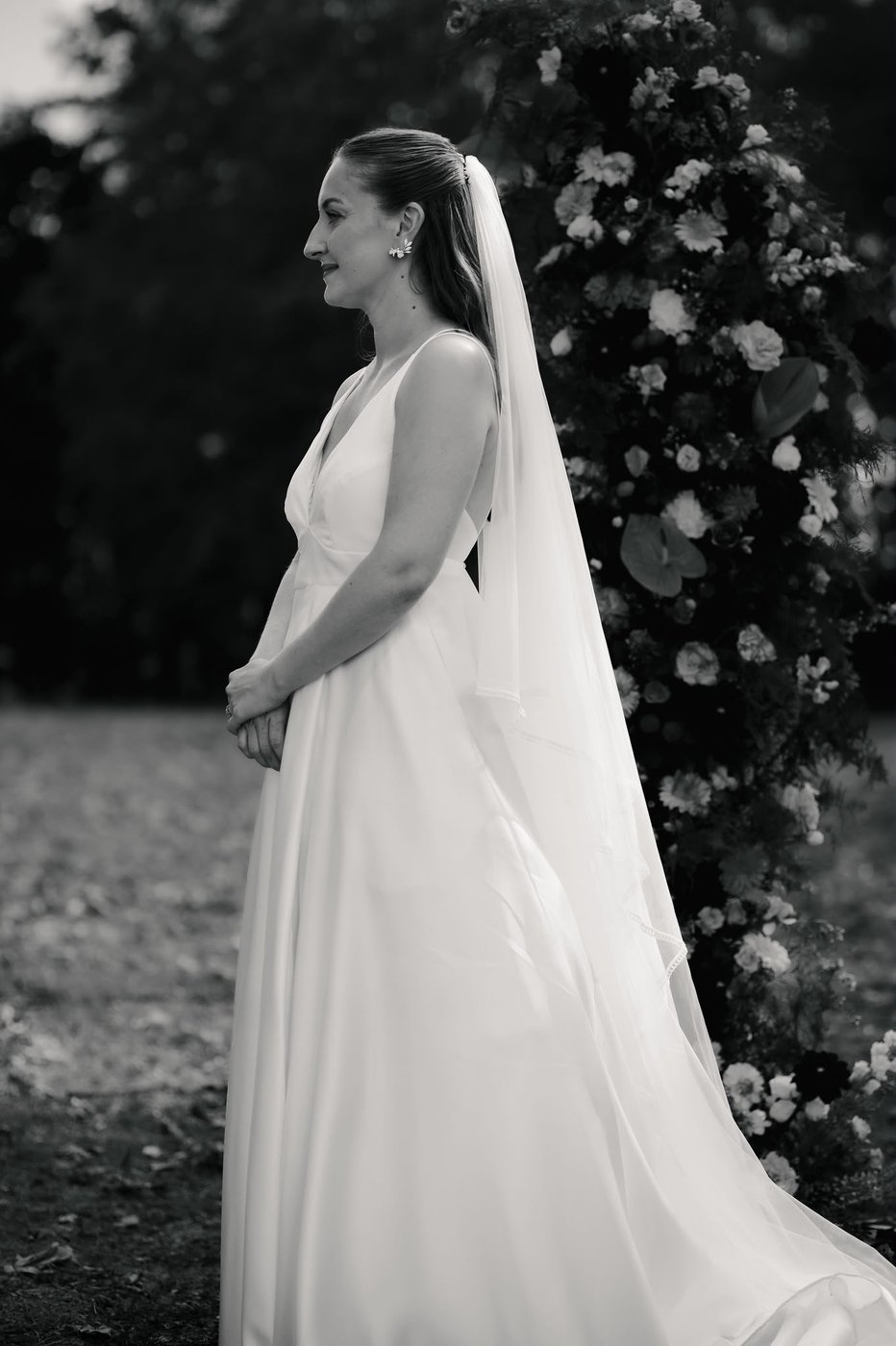 Mariée de profil avec voile devant une arche florale, noir et blanc