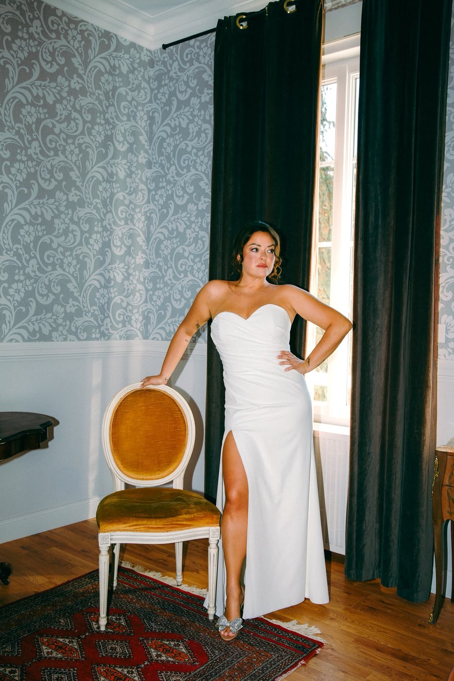 Mariée en robe fourreau fendue posant près d'un fauteuil doré